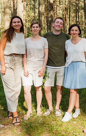 Four people standing together and smiling in a sunny forest setting.